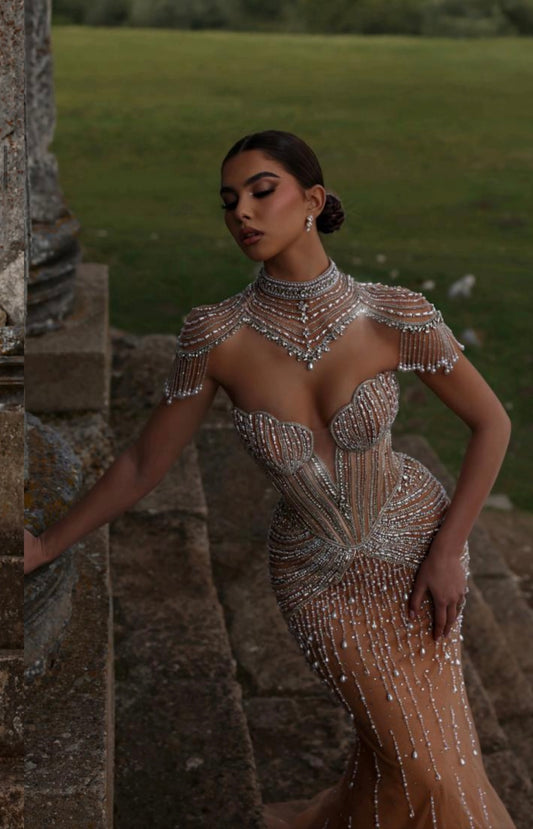 Dress embellished with sparkling crystals and gemstones, featuring a high neckline with jewelry draping from the shoulders.”